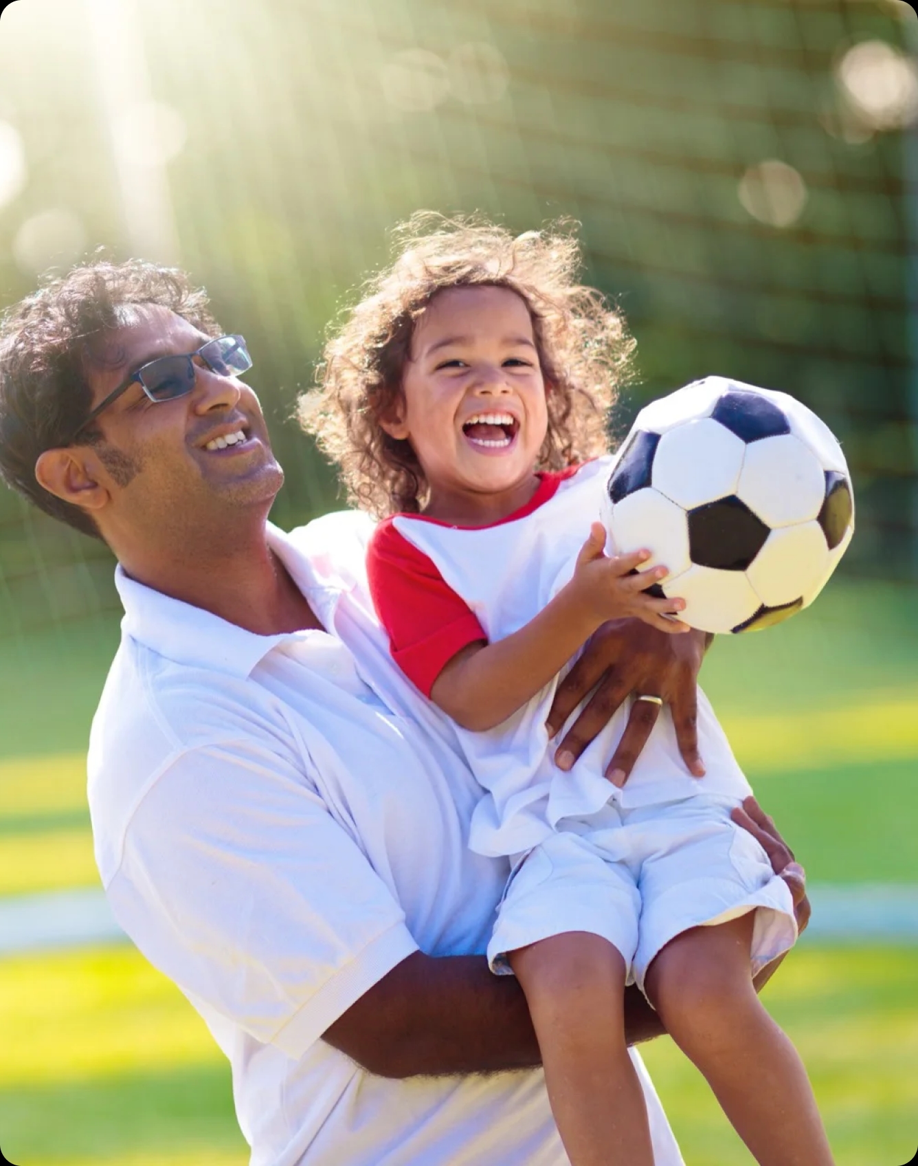 Criança nos braços do pai segurando uma bola de futebol
