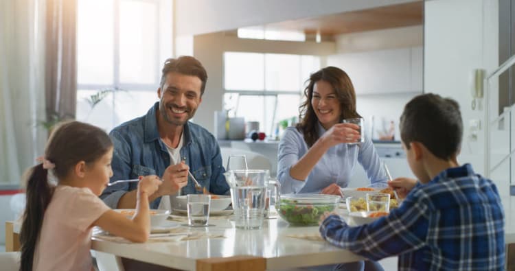 Uma familia comendo sorridente na mesa de jantar