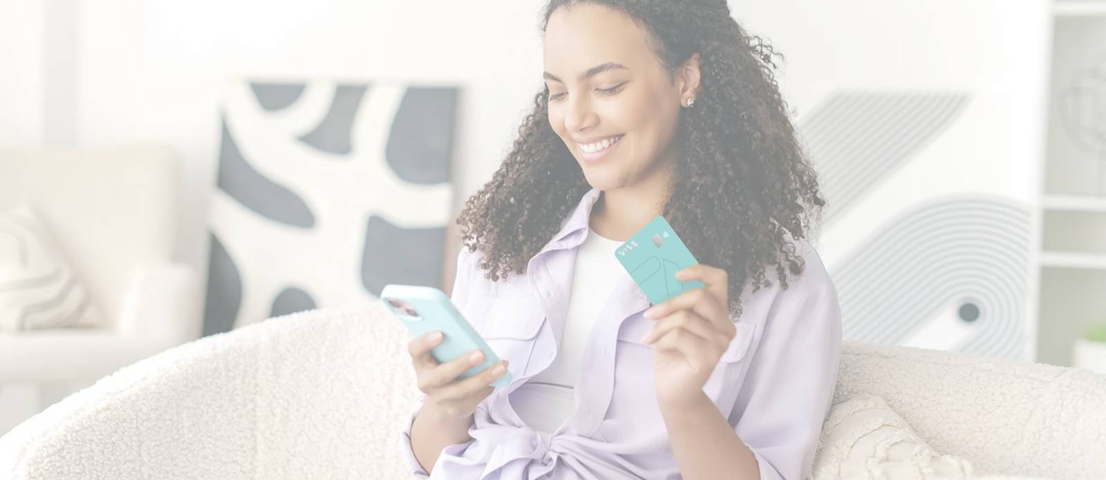 Jovem sentada sorrindo enquanto segura o celular em uma mão e o cartão de benefício METTAcard na outra