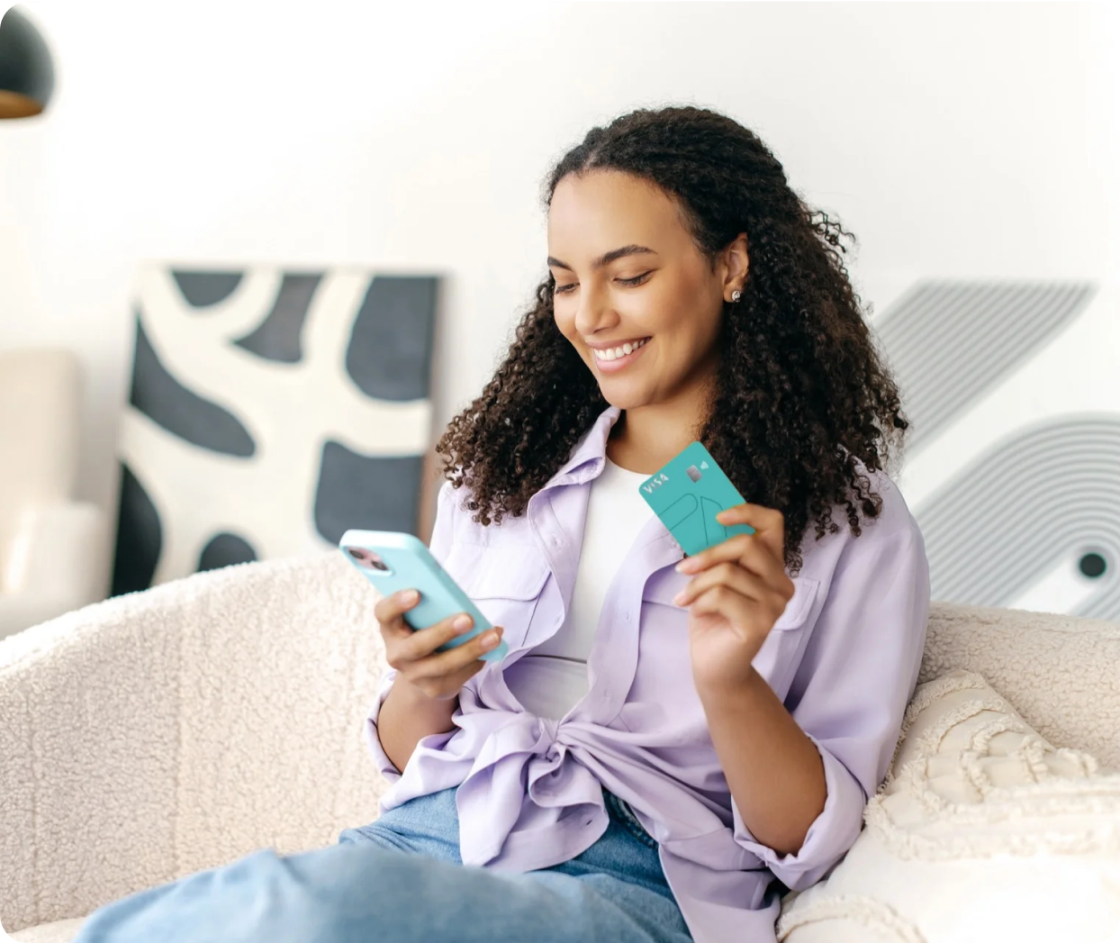 Na imagem você vê uma jovem negra com um belo cabelo cacheado e um belo sorriso enquanto segura o METTAcard em uma mão e acessa o aplicativo com a outra utilizando o celular